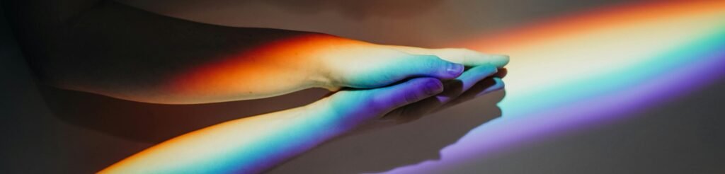 Two diverse hands touch under a rainbow light symbolizing unity and diversity.